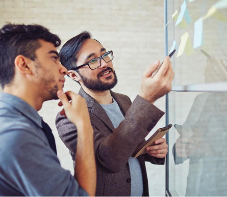 Two people standing next to each other looking at sticky-note papers stuck to a window.