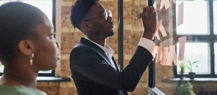 A man writes on sticky-note paper stuck to a window as a woman watches.