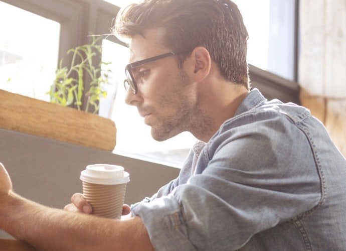 A man reads something on a smartphone while holding a paper coffee cup.